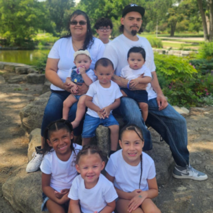 Alicia's family smiling in matching white t shirts and blue jeans.